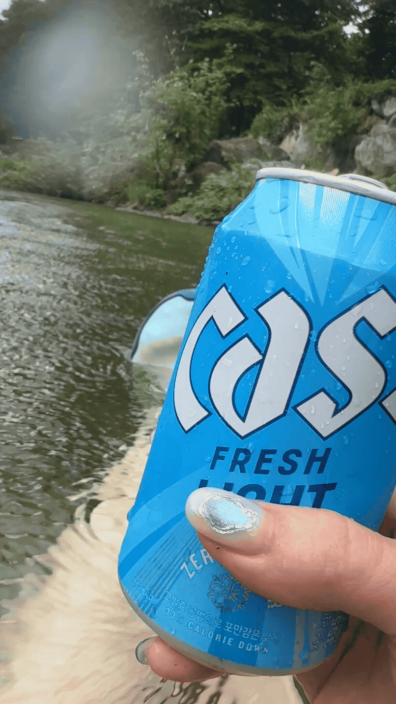 가평 계곡 물속에서 카스 라이트 맥주를 들고 있는 모습. 시원한 물결과 산 풍경이 함께 어우러져 여행 분위기를 살려준다.