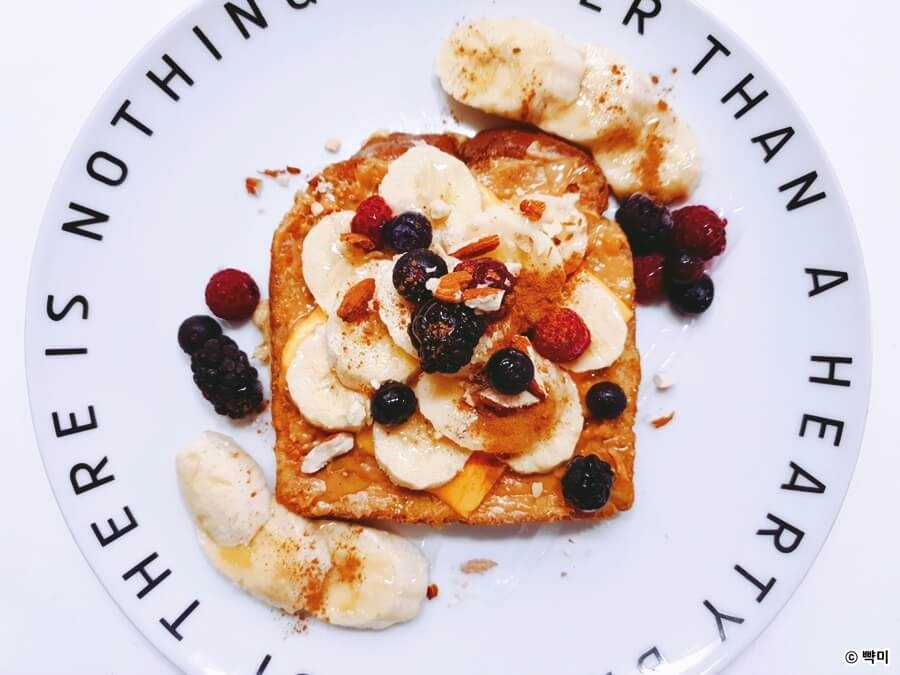 바나나를 썰어 식빵 위에 올리고 견과류와 베리류로 토핑한 프렌치토스트 완성 모습