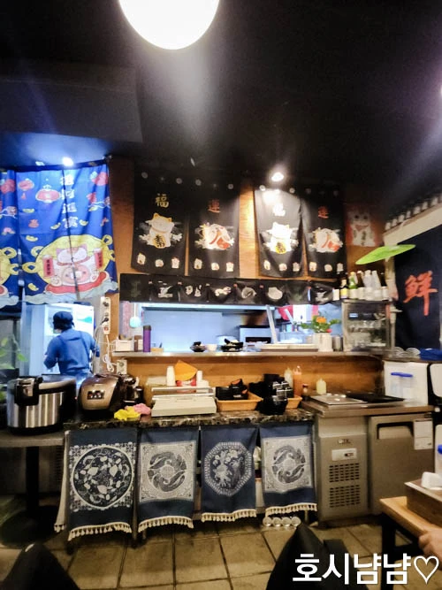 하남 920숙성회 내부 인테리어 - 주류 냉장고와 조리 공간이 보이는 따뜻한 분위기의 실내