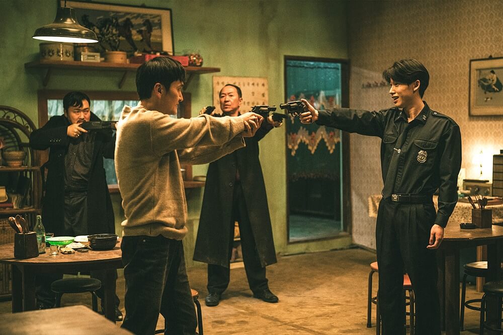 영화 더 킬러스 스틸컷 – 서로 총을 겨누며 진실과 생존의 경계가 무너지는 상징적인 장면