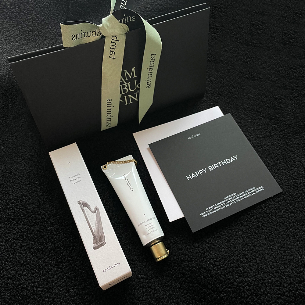 위에-연두-색상의-탬버린즈가-기재된-리본-끈이-달린-검은-색상의-패키지가-있습니다.-좌측에-7이-기재된-핸드크림-박스,-7이-기재된-금색-뚜껑의-핸드크림,-happy-birthday가-기재된-검은-색상의-종이가-있습니다.