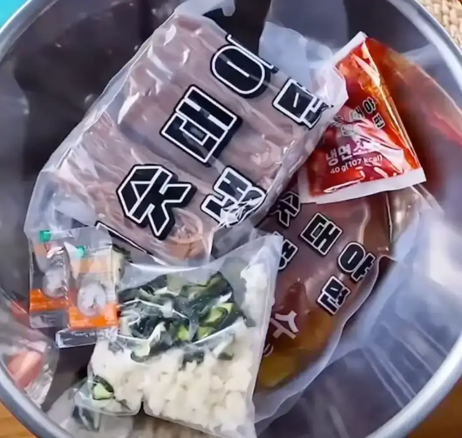 스테인레스 용기안 비닐에 담긴 냉면면발과 야채봉지, 육수봉지와 소스봉지