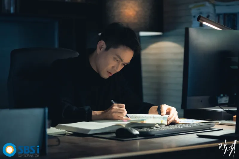 야밤에 사무실 책상에 앉아서 무언가를 펜으로 체크하면서 알아보고 있는 염해상