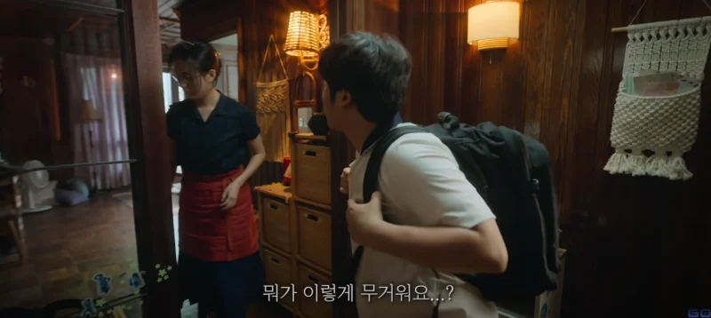 실내를 배경으로 무거운 가방을 메고 있는 김봉석과 앞치마를 두르고 있는 이미현