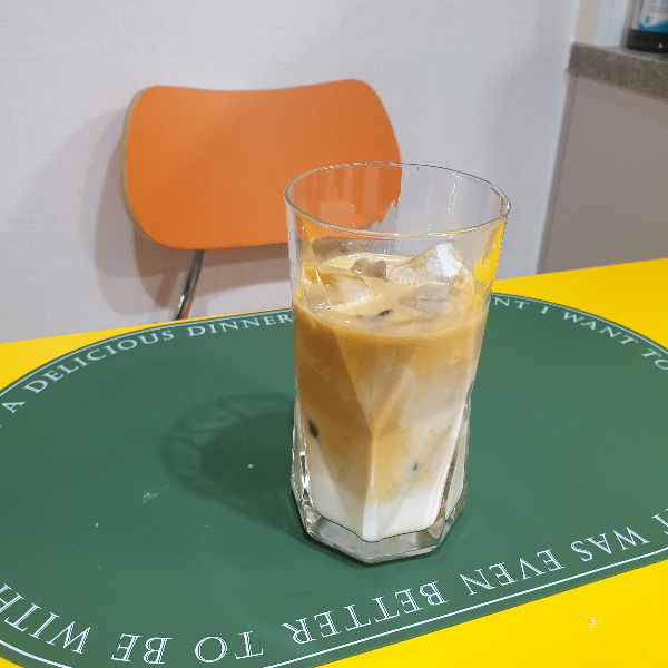 노란 테이블 위에 초록 매트가 깔려 있고 그 위에 아이스 라테가 올려져있다.
