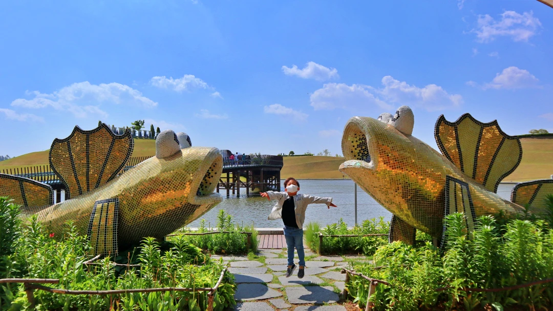 파란하늘에 호수가 있다. 그 앞에 짱뚱어 두마리가 양쪽에 있고 그 사이에서 한 아이가 점프를 한다.