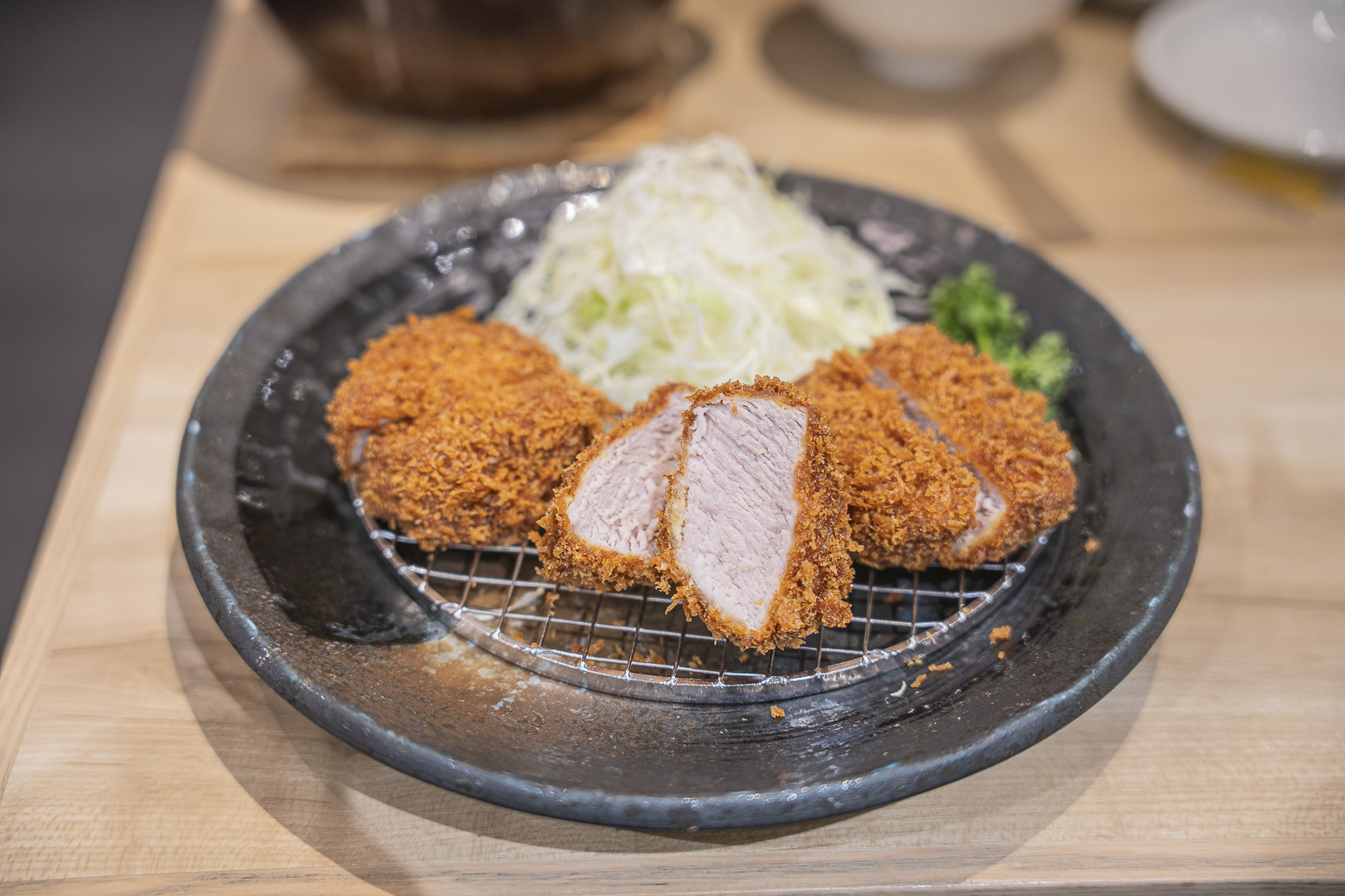 Tonkatsu Kagurazaka Sakura, AEON Mall Kitaoji: sliced pork cutlet on a rack over a black plate, with its cross section and cabbage visible.