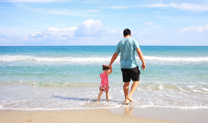 바닷가에서 손을 잡고 걷는 아빠와 어린 딸, 여름 휴가의 따뜻한 가족 순간
