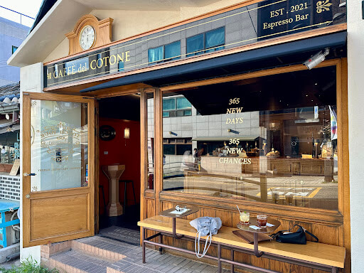 서울 북촌에 위치한 카페 델 꼬또네 외관. 유럽풍 에스프레소 바 스타일의 입구와 나무 벤치 위 음료가 놓여 있으며&amp;#44; 창문에는 &amp;#39;365 NEW DAYS&amp;#44; 365 NEW CHANCES&amp;#39; 문구가 새겨져 있음.