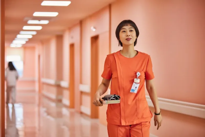 정신병동 복도를 배경으로 오렌지색 간호사 복장에 쇼컷 머리를 하고 있는 드라마 정신병동에도 아침이 와요의 홍정란 캐릭터