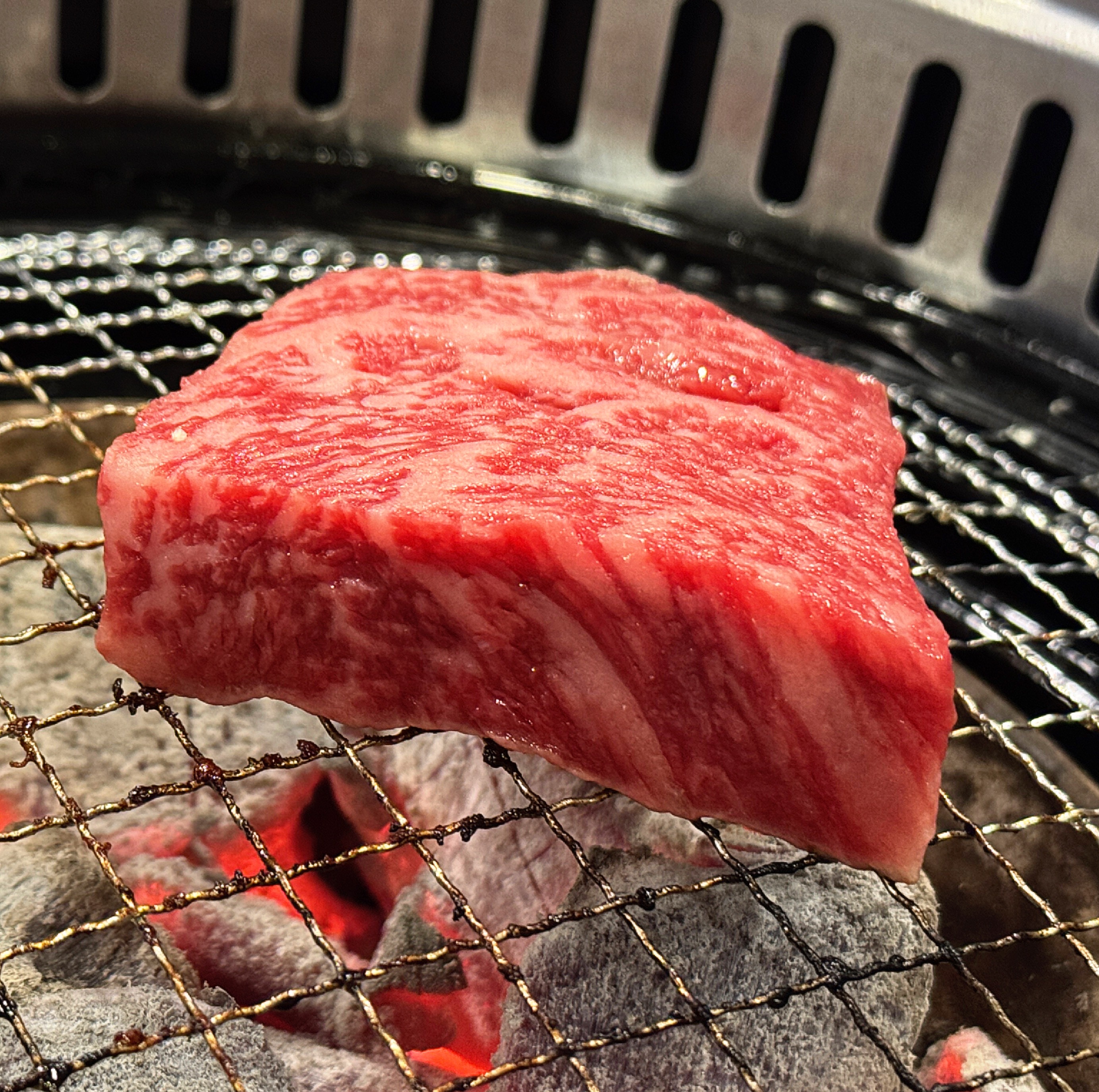 삼거리 명품한우에서 두툼한 소고기 한 점이 숯불에 올려져 구워지고 있는 클로즈업 장면. 마블링이 살아 있는 고기의 질감이 생생하게 보인다