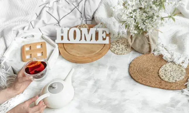 살림템으로 꾸며진 아늑한 공간에 티포트, 차, 홈 장식 소품, 러그와 꽃 등이 배치된 따뜻한 홈 인테리어 이미지