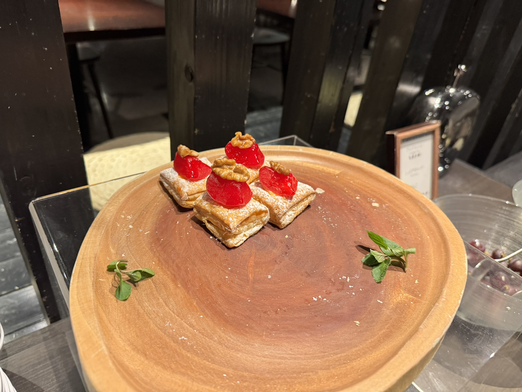 바삭한 페이스트리 위에 빨간 젤리와 호두가 토핑된 한입 크기의 디저트가 나무 쟁반 위에 놓여 있는 클로즈업 사진.