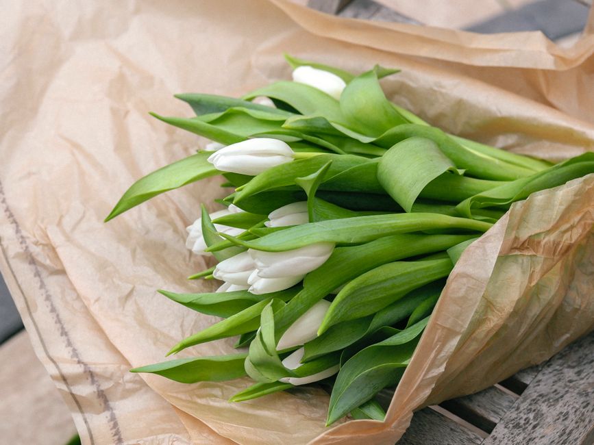 A bouquet of white tulips wrapped in kraft paper, showcasing elegance and simplicity.