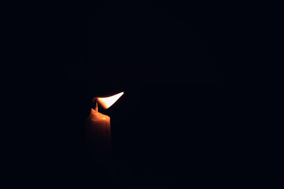 A single burning candle illuminates the darkness, casting a warm glow.