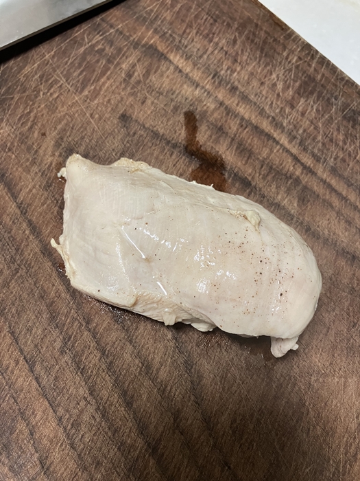 삶기 완료 후 도마 위에 올려진 통 닭가슴살, 겉면의 윤기가 살아 있는 상태
