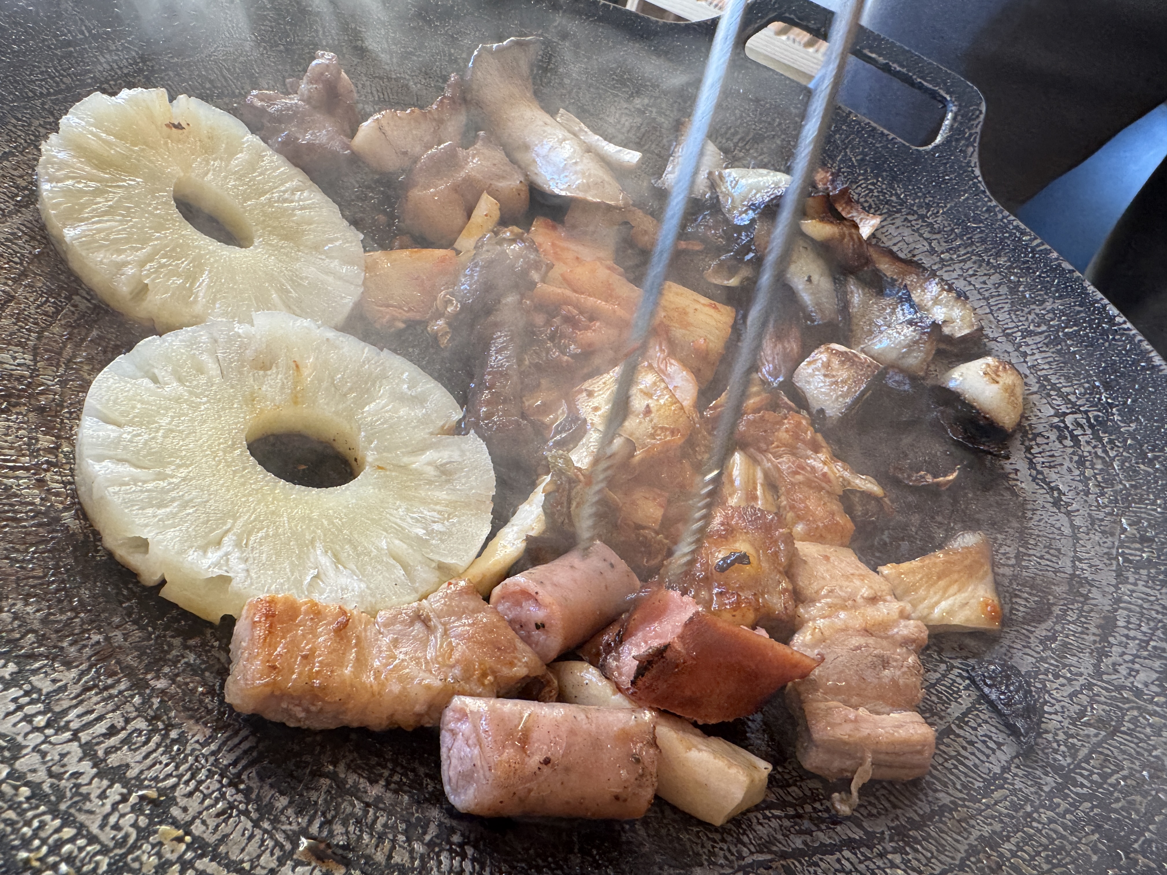 바베큐 불판 위에서 돼지고기와 함께 굽고 있는 파인애플 링&amp;#44; 불에 구워 단맛이 살아난 캠핑 바베큐 사이드 메뉴