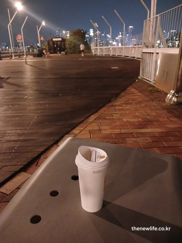 야간 한강 산책로 벤치 위에 운동후 마시는 테이크아웃 커피 컵