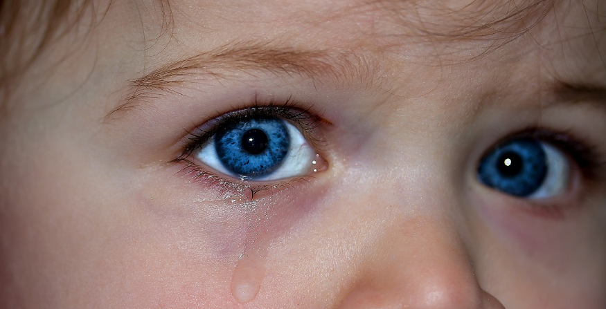 푸른 눈을 가진 어린아이가 눈물을 흘리며 아픈 표정을 짓고 있는 모습