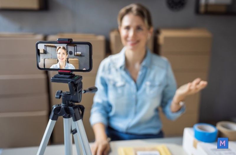 소상공인이 스마트폰으로 SNS 마케팅 영상 콘텐츠를 제작하는 모습 - 삼각대에 고정된 스마트폰으로 촬영 중인 여성 사업자 via canva