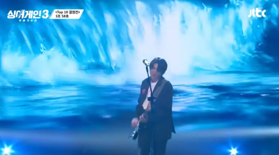 싱어게인3-
파도가 몰아치는 무대화면 배경 남색쟈켓&#44; 웨이브진 머리 흰색면티 전기기타를 치며 스탠딩 마이크앞에서 노래하는 58호