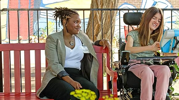 Out of My Mind 영화 장면, 멜로디가 교사와 함께 벤치에 앉아 보조기기로 대화하는 모습