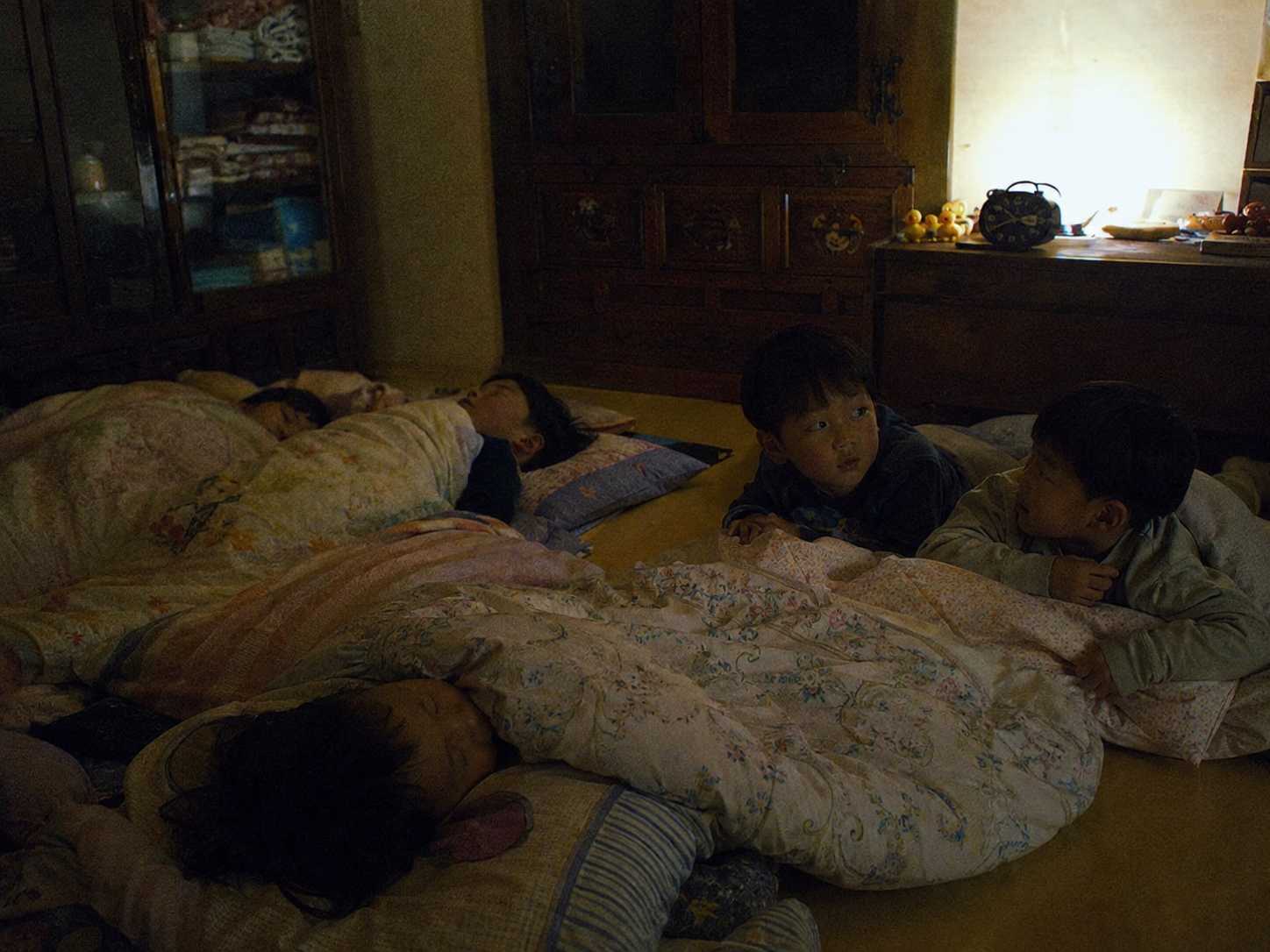 어두운 친척집 방에서 이불을 덮고 누워 아직 잠들지 못한 아이들의 모습