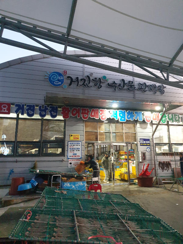 어둠이 살짝 깔린 하늘 거진항 수산물 판매장이라는 간판이 있는 건물이 보인다.