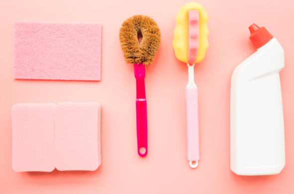 분홍 배경 위에 가지런히 놓인 다양한 주방 수세미와 세정제 병