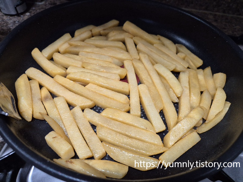 Frozen french fries being sautéed in a frying pan on a stovetop