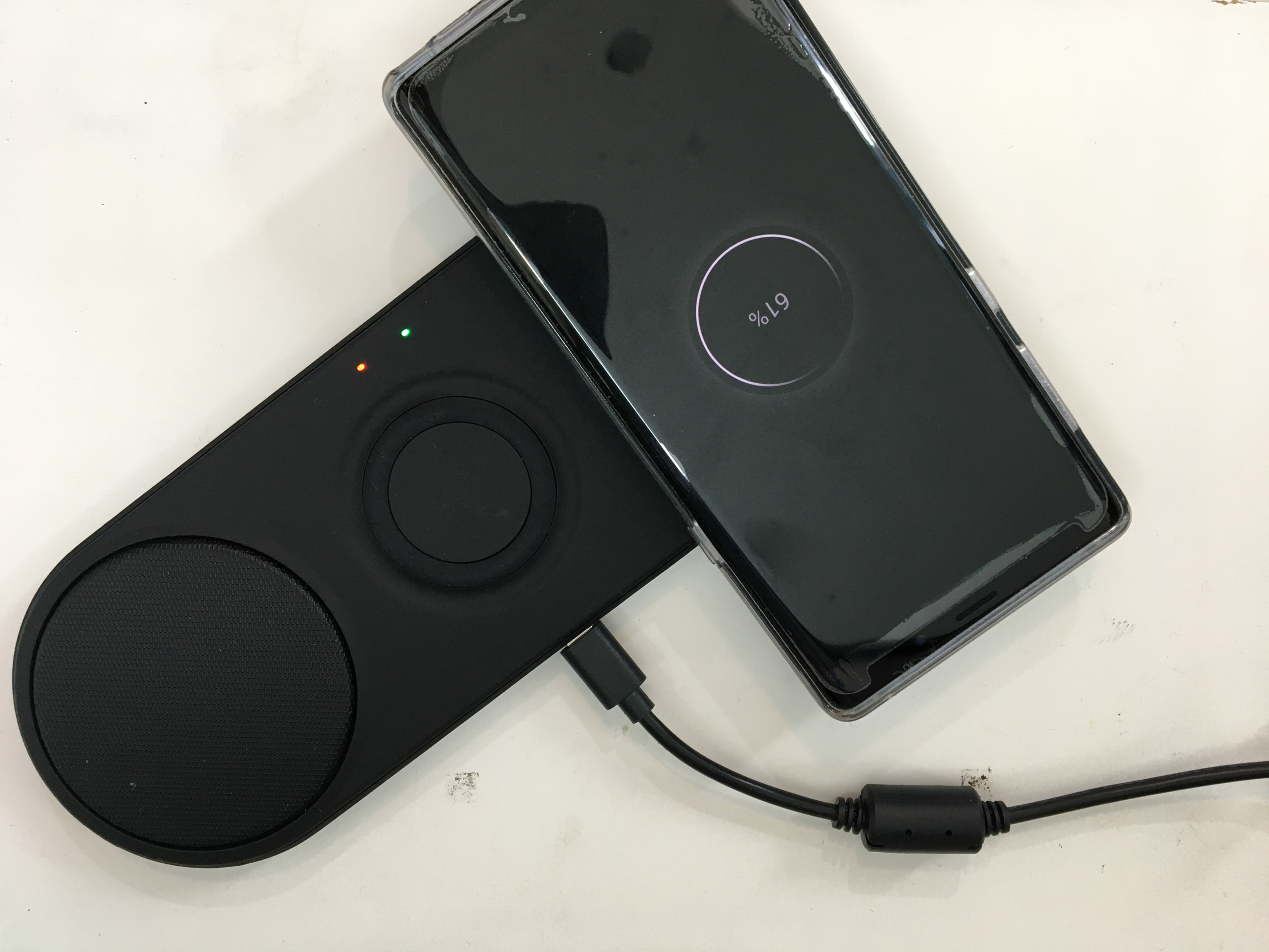 스마트폰이 CAROTA 3-in-1 무선 충전패드 위에서 무선 충전 중이며, 녹색과 주황색 LED 표시등이 켜져 있다.