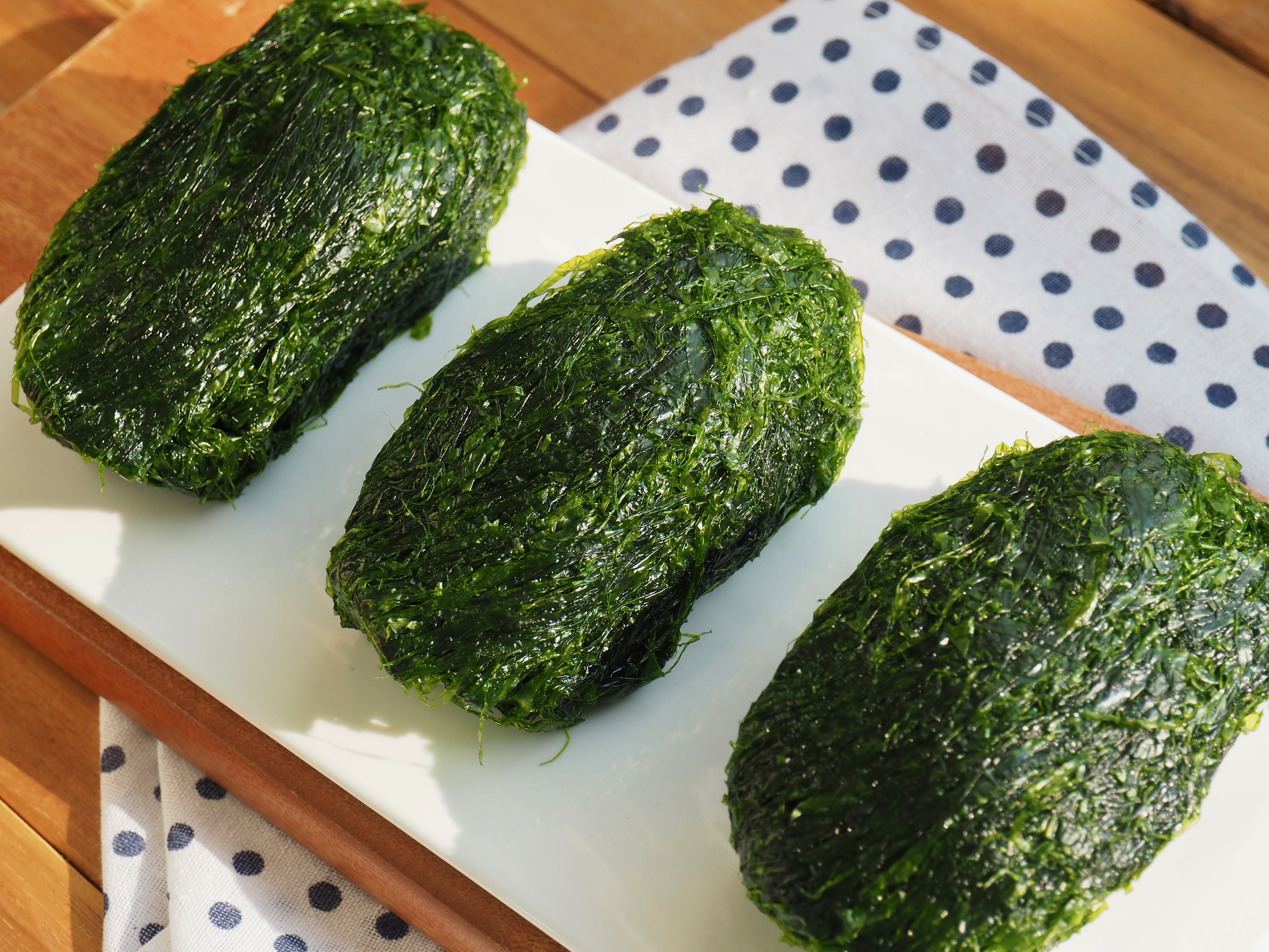 바다에서 채취를 한 파래를 잘 세척한 후에 커다랗게 3덩어리로 뭉쳐서 나무 바닥 위에 흰색의 네모난 접시 위에 나란히 놓고 찍은 사진