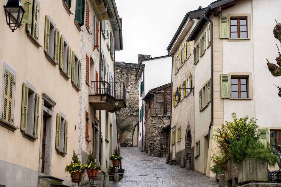 Quaint narrow street in Swiss village with historic stone buildings and wooden shutters.