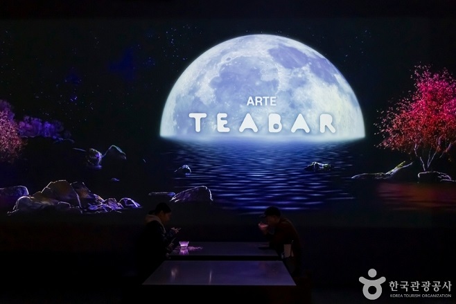 어두운 화면에 붉은 나무와 다바에 비친 반달의 모습이 벽면에 전시된 모습