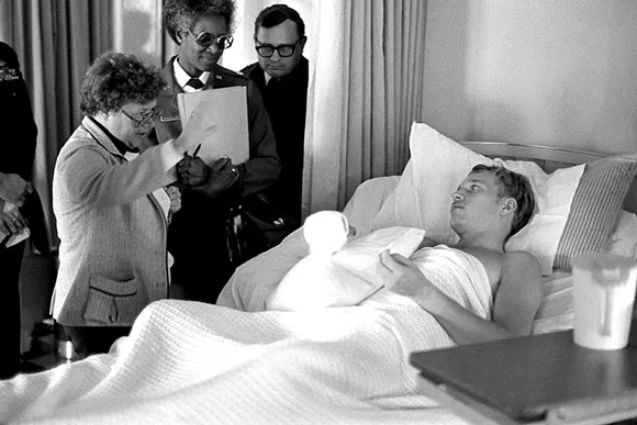 병원 침대에 누워 있는 사람과 대화 중인 중년 여성