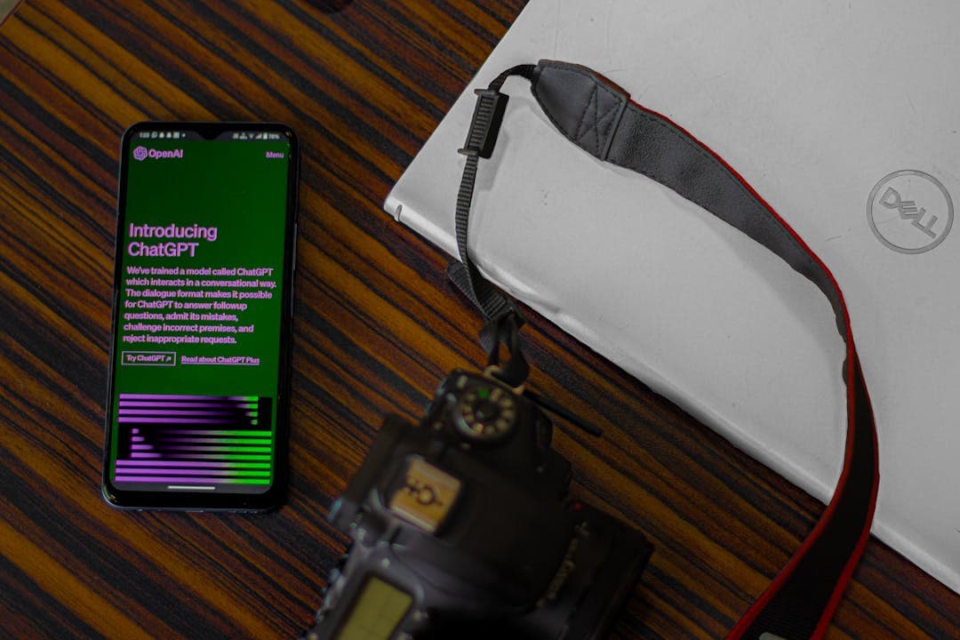 챗GPT 소개 화면이 표시된 스마트폰&amp;#44; 옆에는 카메라와 델 노트북이 놓인 책상