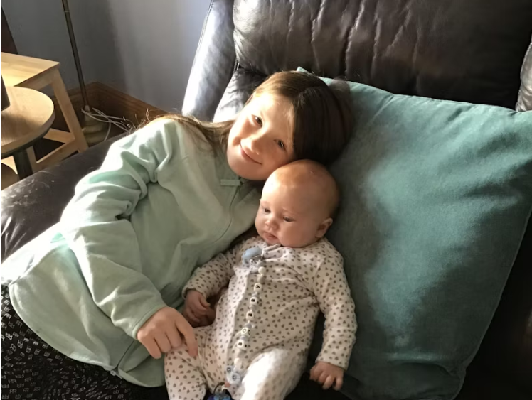 소파에 나란히 앉아 있는 어린 형제와 신생아의 따뜻한 가정 모습