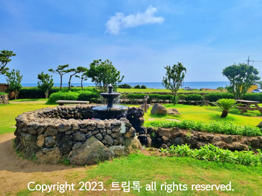돌담 너머 바다가 보이고 그 안에 둥그렇게 쌓인 현무암 돌벽과 분수대의 모습