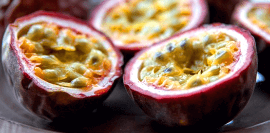 빨간 껍질을 가진 패션후르츠를 반으로 자른 모습으로 노란 알갱이들이 가득하다.