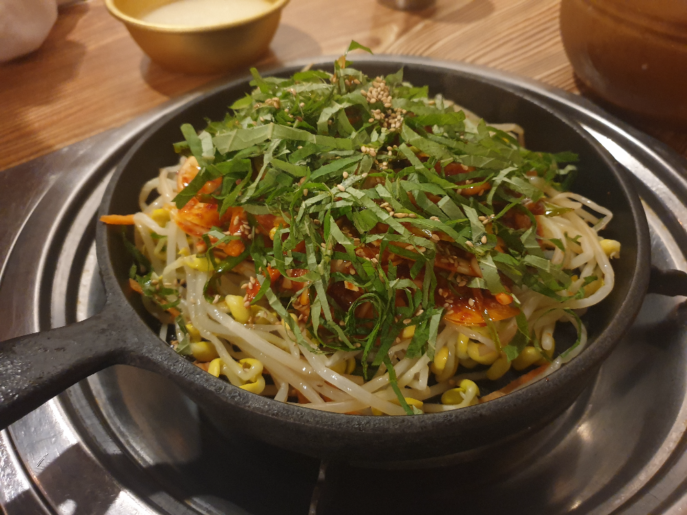 테이블 위에 닭발 볶음이 들어있는 팬이 놓여져 있다. 그 위에 막걸리 사발도 보인다.