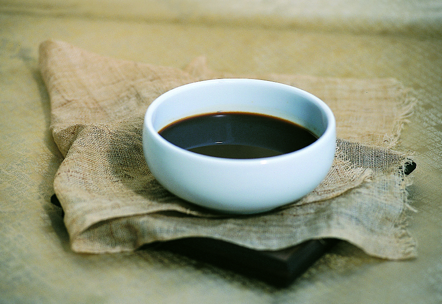 야생에서 채취를 한 각종 한약재를 물과 함께 혼합을 하여 끓인 것을 잘 짜낸 한약을 동그랗고 하얀 그릇에 반쯤 담아두고 금색 바닥 위에 삼베를 깔은 네모난 쟁반 위에 놓아두고 찍은 사진