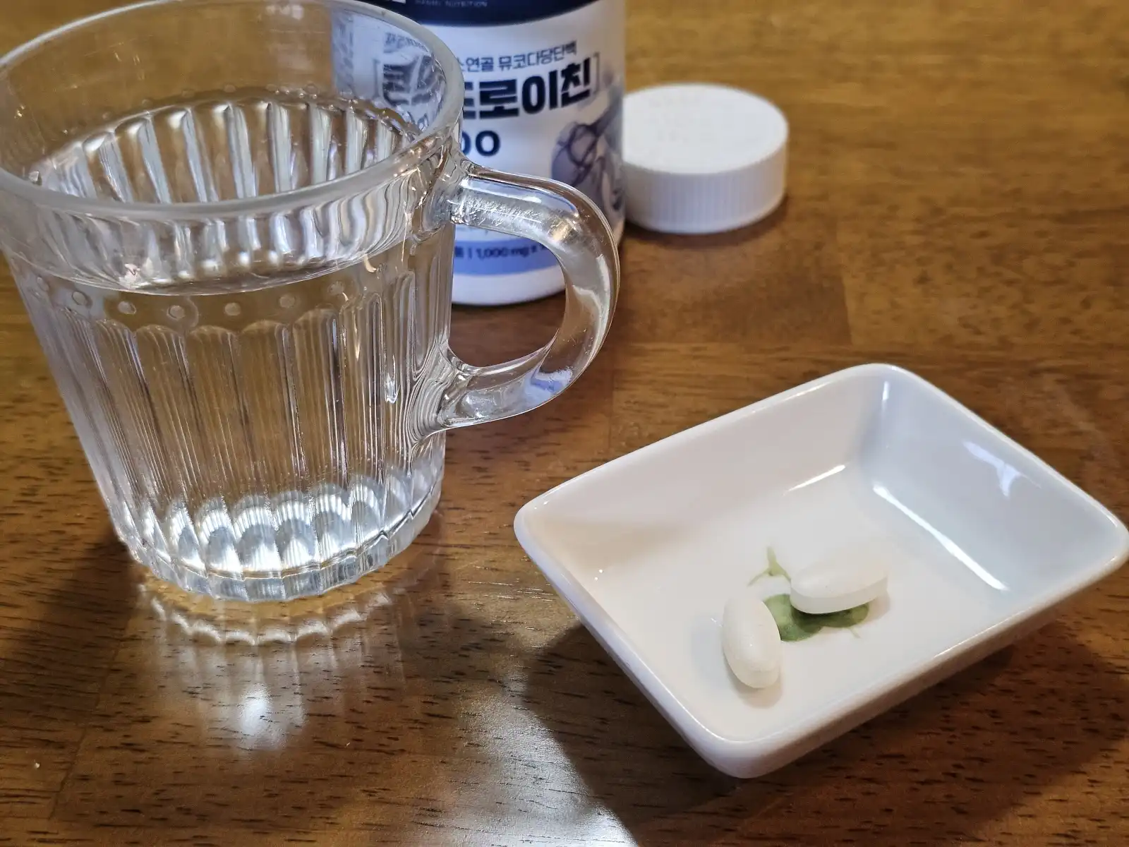 물 한 잔과 함께 예쁜 접시에 담긴 영양제