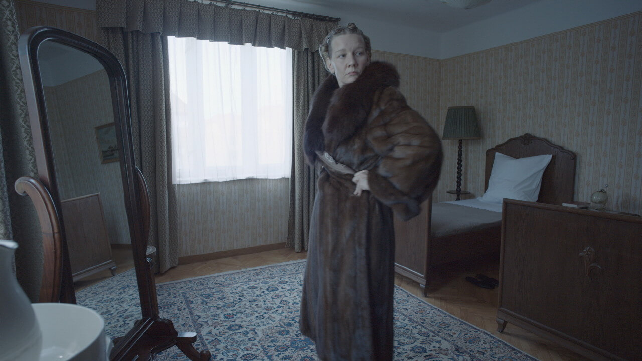 수용소에서 나온 물품인 모피 코트를 입고 거울을 보며 포즈를 취하는 산드라 휠러