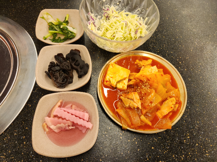 샐러드와 김치찌개, 나물과 버섯이 담긴 접시가 테이블 위에 올려져 있다