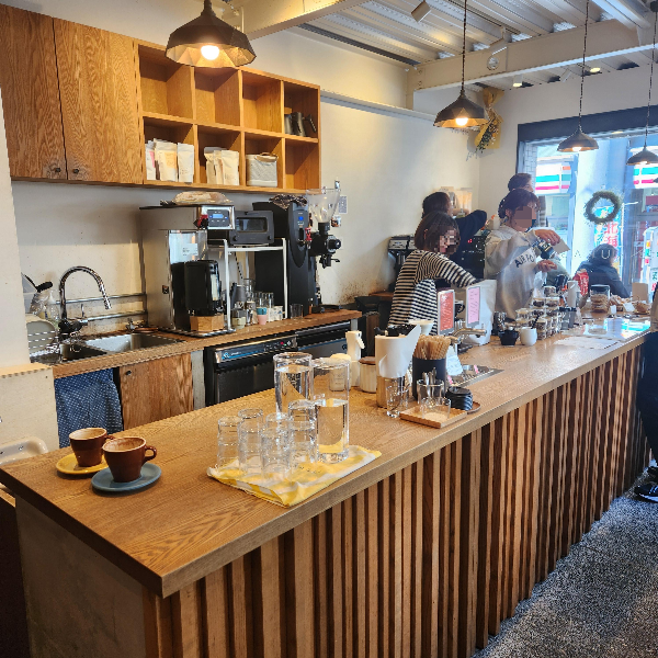 흰 벽과 우드 인테리어로 깔끔한 내부. 여러 바리스타가 커피를 추출 중이다.