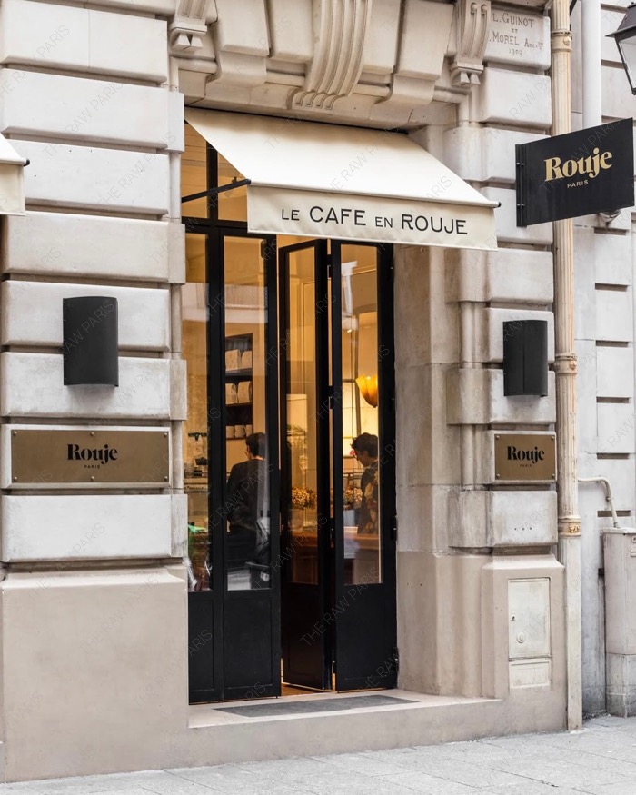 The elegant stone facade of Le Cafe en Rouje with cream awning and black Rouje signs in Paris