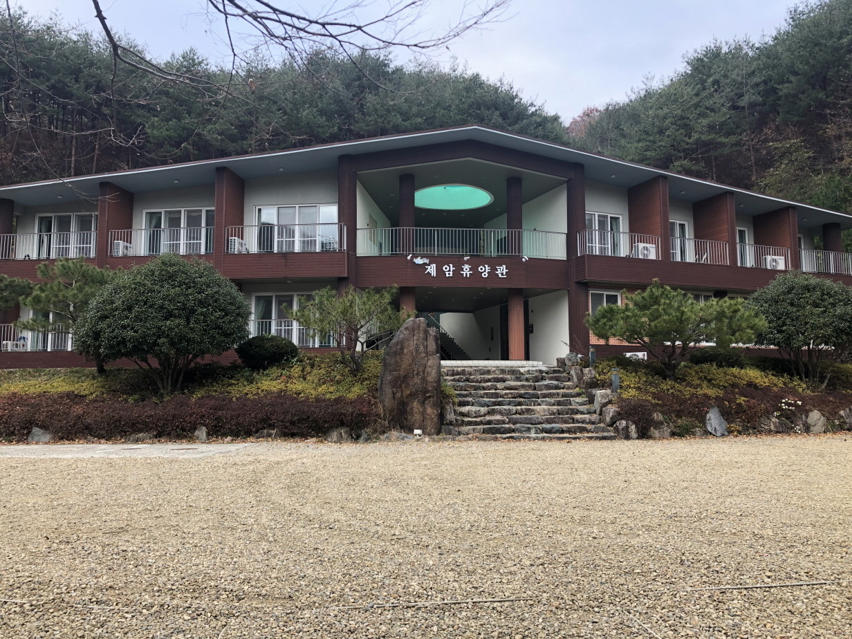 제암산의 웅장한 기암괴석 아래 울창하게 펼쳐진 숲을 배경으로, 정갈하고 현대적인 외관을 자랑하는 제암휴양관(연립동) 건물의 평화로운 전경
