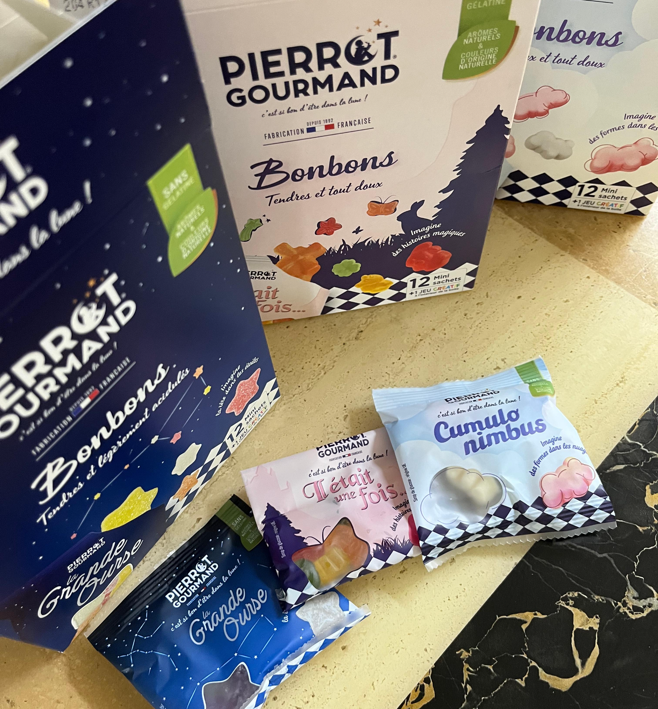 프랑스 비건 젤리 브랜드 '피에로 구르망(Pierrot Gourmand)'의 대형 패키지 상자들과 그 앞에 놓인 3가지 종류의 미니 소포장 파우치(원스 어폰 어 타임, 그레이트 베어, 큐물로 님부스) 실물 사진. 감성적인 별자리 디자인의 네이비, 핑크, 스카이블루 패키지가 고급스러운 대리석 테이블 위에 연출되어 있다.