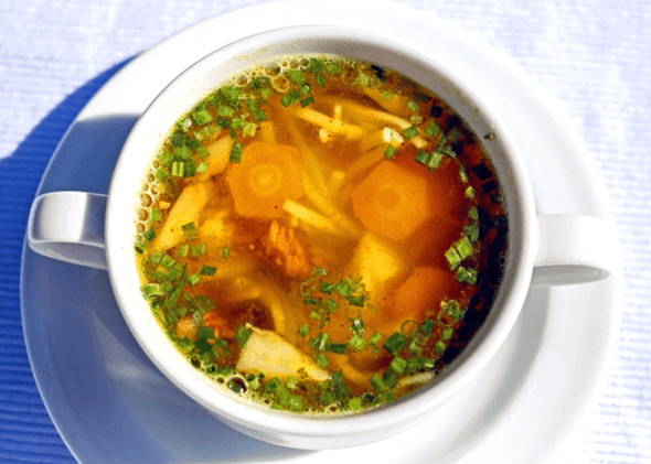 하얀 그릇에 야채가 가득한 국이 있다. 당근, 파, 감자가 있는 국이다.