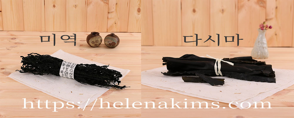 나무 탁자 하얀 종이 위에 왼쪽에는 마른 미역 묶음이, 오른쪽에는 마른 다시마 묶음이 놓인 이미지.